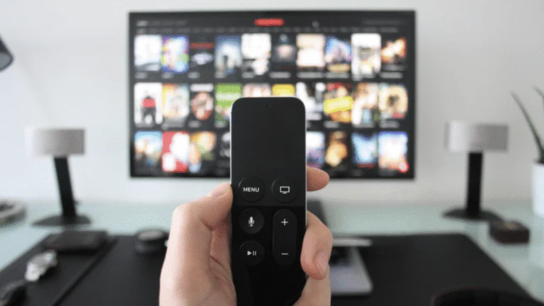 Hand holding a remote control in front of a smart TV displaying streaming content, showcasing IPTV Smarters Pro interface